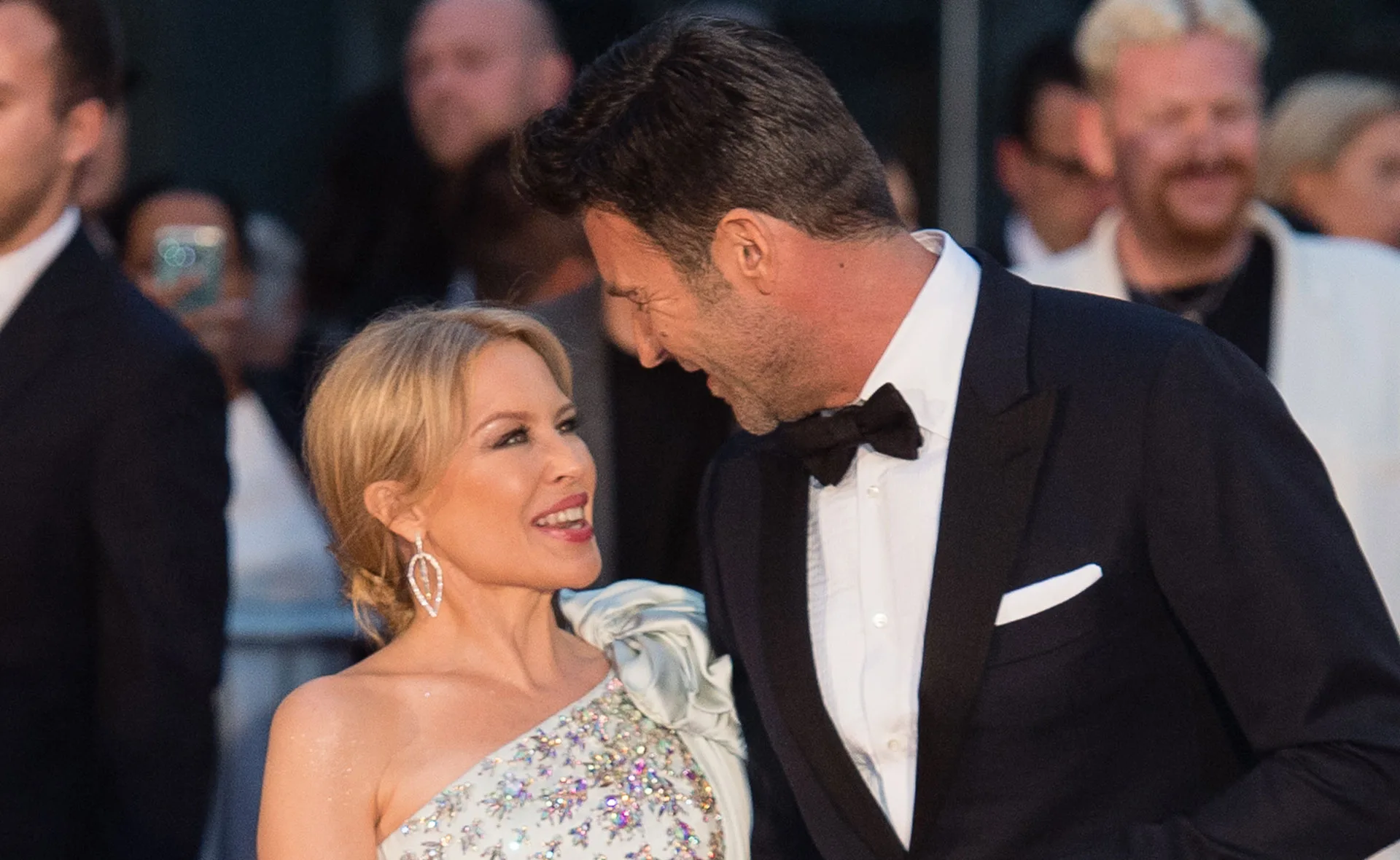 alt="A couple smiling warmly at each other, dressed in elegant formal attire at a public event."