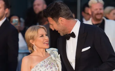 alt="A couple smiling warmly at each other, dressed in elegant formal attire at a public event."