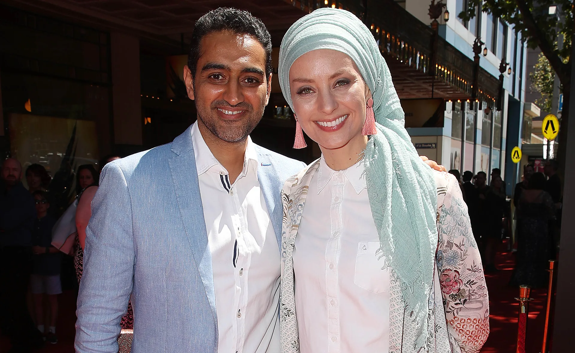 A smiling couple in formal attire poses on a red carpet.