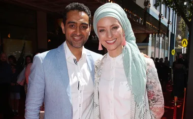 A smiling couple in formal attire poses on a red carpet.