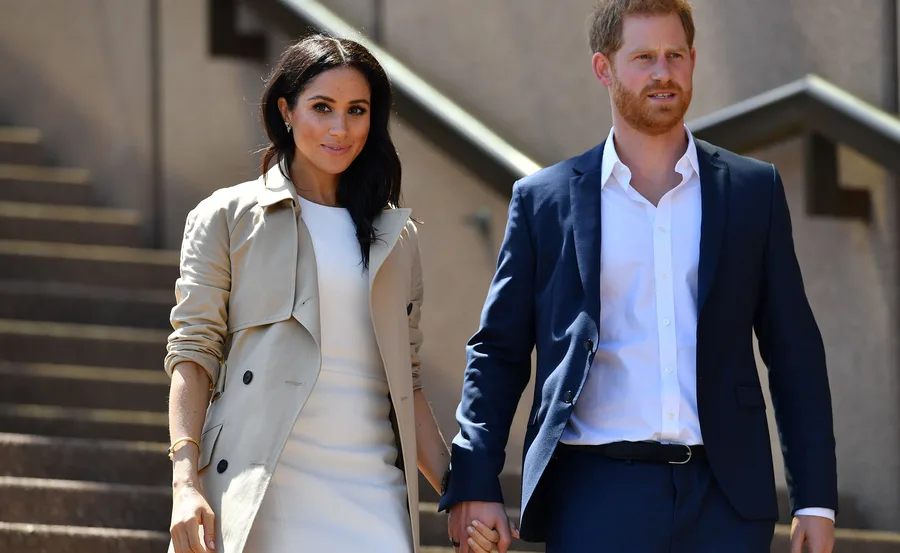 Prince Harry and Meghan Markle walking hand in hand, dressed formally.