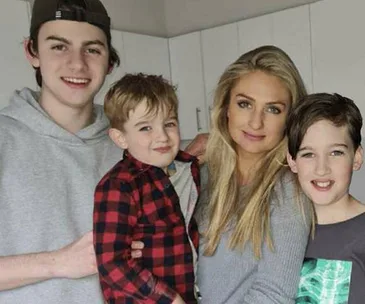 Group photo of a woman and three children smiling in a kitchen setting.