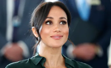 A woman with long dark hair wearing a dark outfit, smiling slightly while looking upwards.