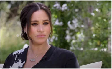 A woman with brown hair sits outdoors, wearing a dark top, with a thoughtful expression.