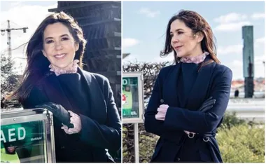 A woman in a dark coat stands beside an automated external defibrillator (AED) outdoors.