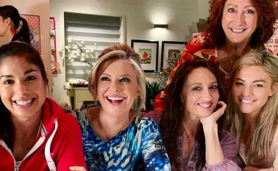 Women from "Home and Away" smiling together indoors, celebrating International Women's Day.