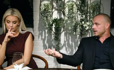 A woman looks pensive while a man gestures emphatically during a discussion at a dining setting.