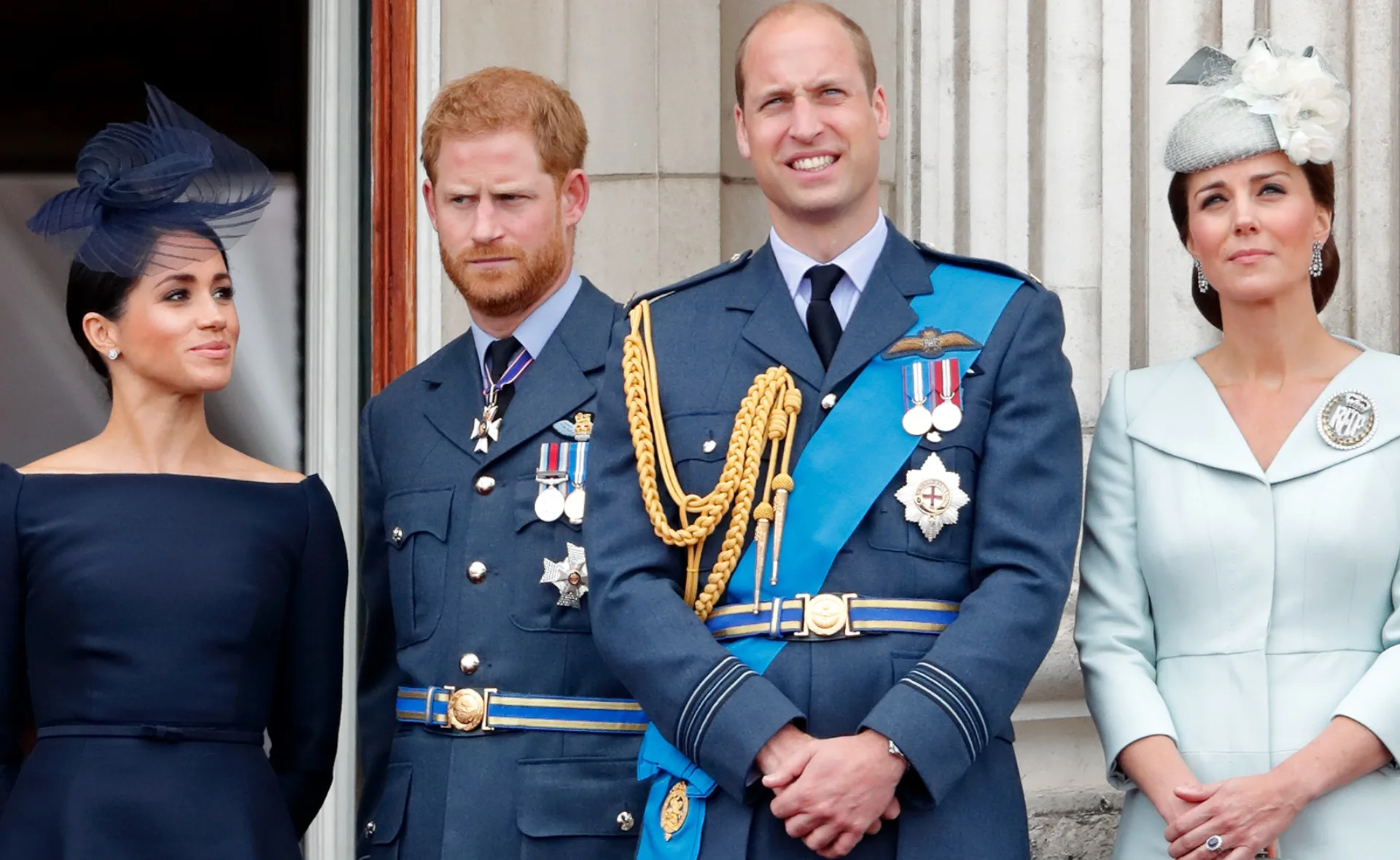 Four people in formal attire stand on a balcony, two in military uniforms.