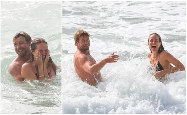 A couple joyfully swims and splashes in the ocean, smiling and laughing amidst the waves.
