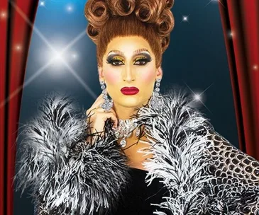 Drag queen in glamorous attire with bold makeup and ornate hairstyle, wearing a feathered coat against a sparkling backdrop.