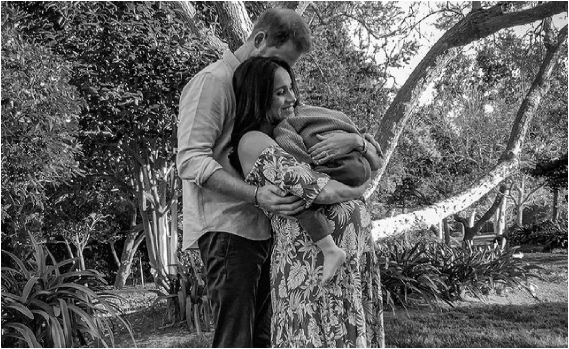 Couple embraces with child in outdoor setting, surrounded by trees and foliage, wearing casual attire.