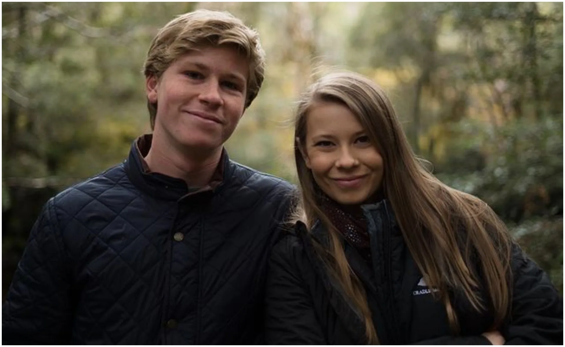 Two people smiling, standing close together in an outdoor setting with trees in the background.
