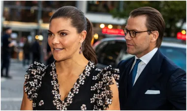 A woman in a floral dress and a man in a suit walk in an urban area, with blurred background lights.