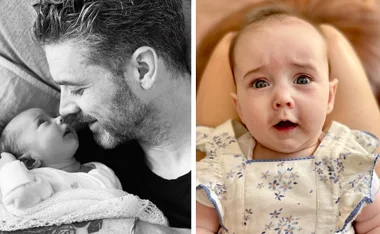 Father and baby daughter sharing a tender moment; baby in floral outfit looks up.