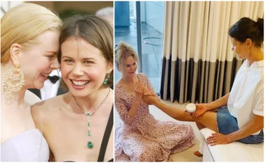 Two women at an event, smiling. One in a formal dress, the other applying lotion to a seated woman's leg indoors.