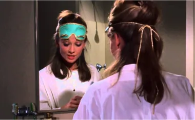Woman in white robe and teal sleep mask looks into a mirror, reflecting her thoughtful expression.