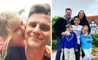 Father poses with daughter kissing his cheek; family of five smiling outdoors with house in background.