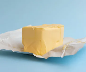 Block of butter on open wrapper, set against a light blue background.