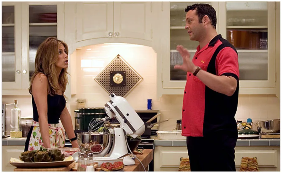 A woman and man discuss in a kitchen with a mixer and food on the counter.