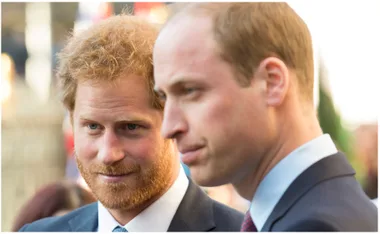 Two men in suits sharing a moment outdoors, one with reddish hair, the other with short light brown hair.