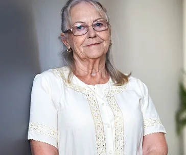 Elderly woman with glasses, smiling gently, wearing a white embroidered blouse, symbolizing osteoporosis awareness.