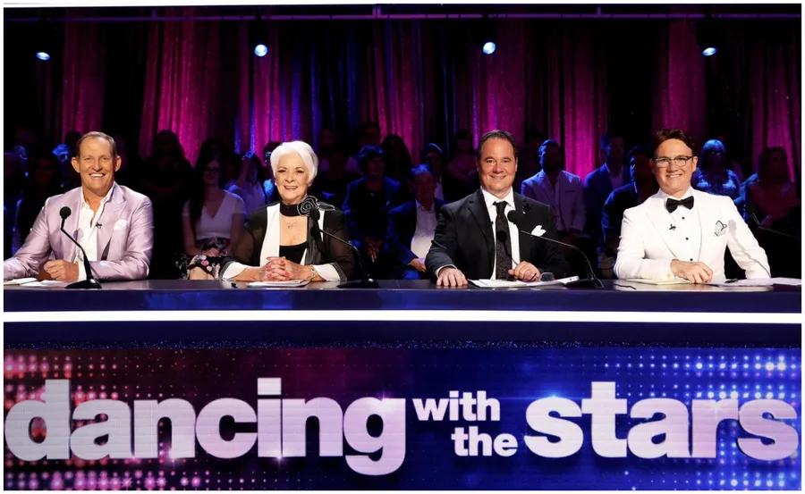 Judges seated at the "Dancing with the Stars" panel, smiling, with a vibrant purple curtain backdrop.