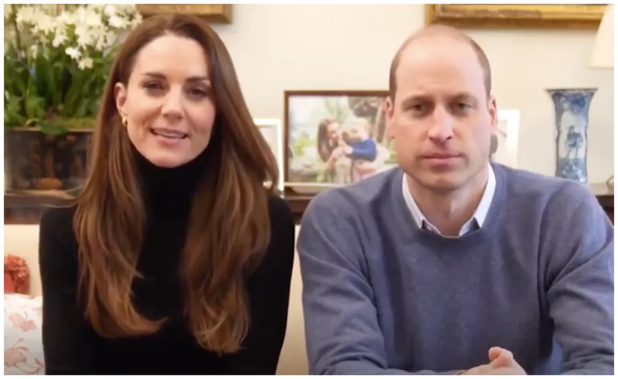 Don't know who they are, but a woman in a black turtleneck and a man in a blue sweater are sitting on a sofa together.