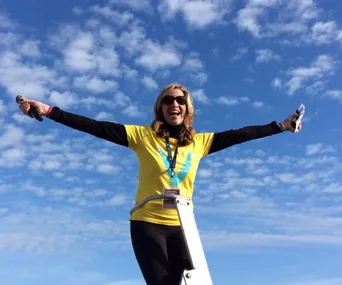 Woman in yellow shirt with arms open wide, smiling under blue sky.