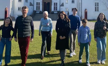 A family walks on grass in front of a white building, enjoying a sunny day.