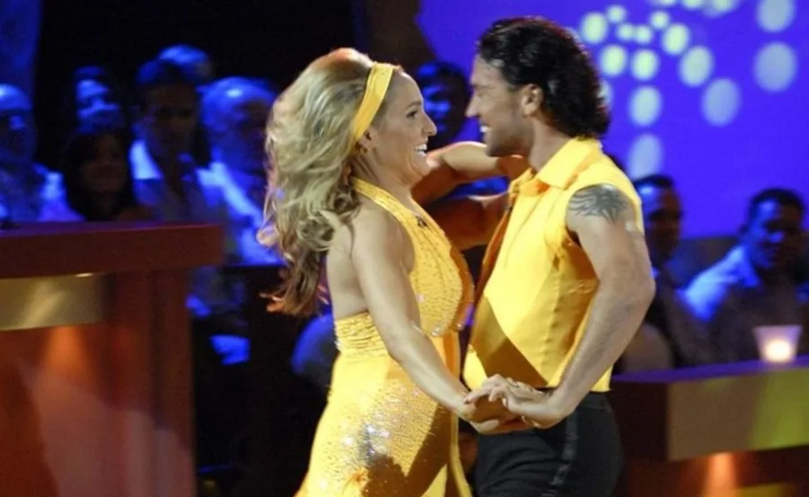 A couple in yellow outfits dancing energetically on a stage with an audience in the background.