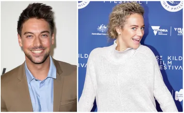 Two people smiling; one in a tan blazer and blue shirt, the other in a light sweater with a festival backdrop.