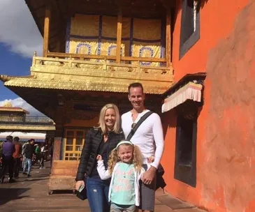 A family poses in front of a traditional building with golden trim and orange walls, under a bright blue sky.