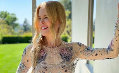 Nicole Kidman wearing a floral embellished sheer dress, smiling outdoors with long wavy blonde hair.