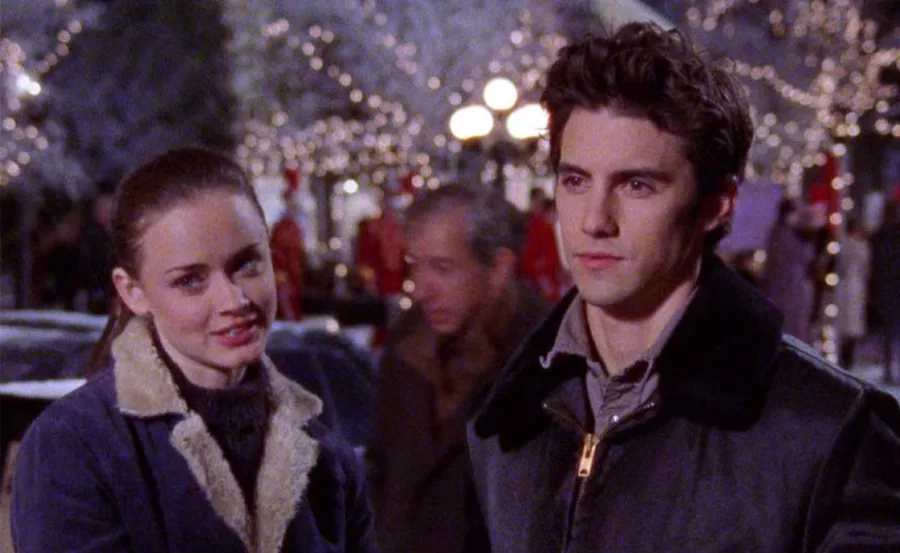 Rory and Jess stand outdoors at night, surrounded by festive lights, in a scene from "Gilmore Girls."
