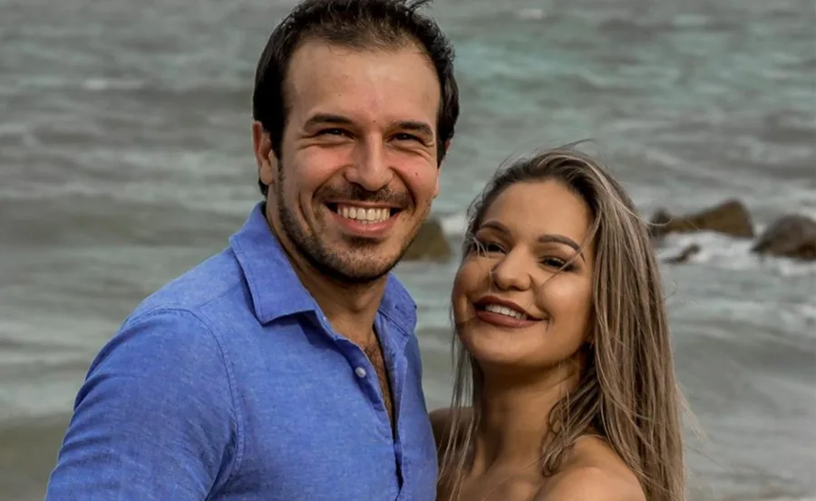 Couple smiling by the ocean with waves in the background.