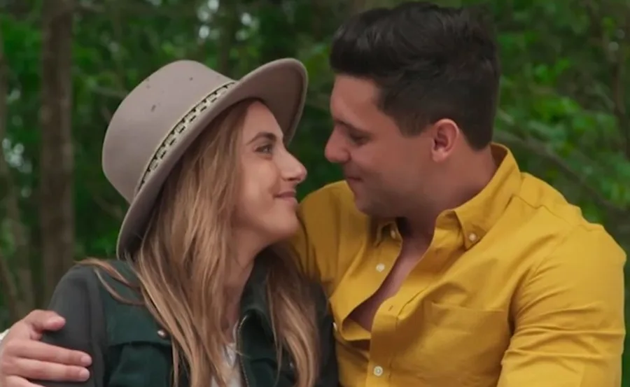 A couple outside, smiling and looking at each other affectionately, with greenery in the background.