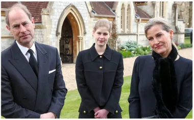 People in formal attire standing outside a stone church, smiling gently.