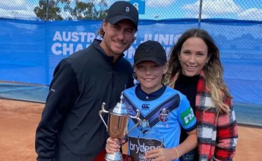 "Three people posing with a tennis trophy on a court."