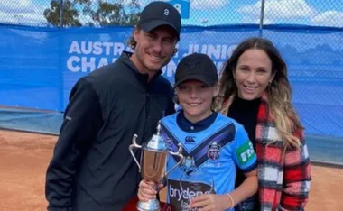 "Three people posing with a tennis trophy on a court."