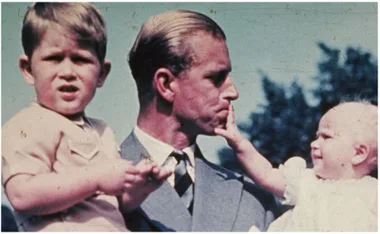 Father in a suit holds two children, one of whom is touching his face, with a clear blue sky in the background.