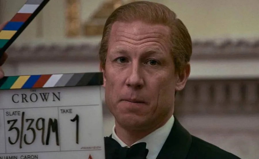 Actor in "The Crown," dressed as Prince Philip, with film clapperboard in the foreground, ready for a scene.