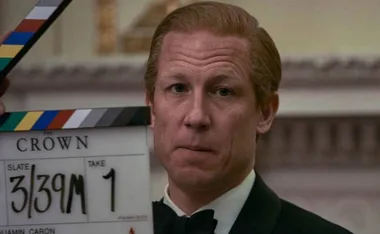 Actor in "The Crown," dressed as Prince Philip, with film clapperboard in the foreground, ready for a scene.