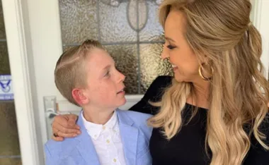 A woman and a young boy smiling at each other outside a house; the boy wears a light blue blazer.