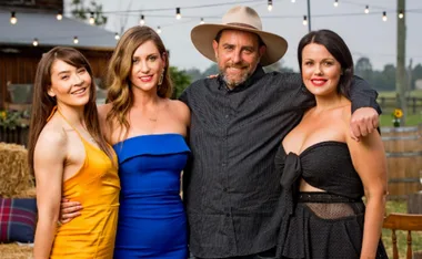 Group photo with a man in a hat and three women in colorful dresses posing outdoors with string lights.