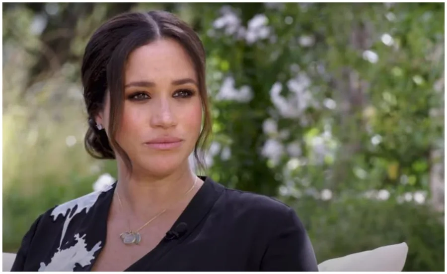 I don't know who is in the image. A woman in black with floral pattern, outdoors, with greenery in the background.