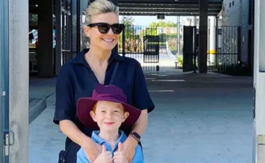 A woman in sunglasses with a young boy wearing a hat, standing in a courtyard.