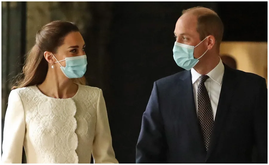 Two people wearing formal attire and face masks, facing each other indoors.