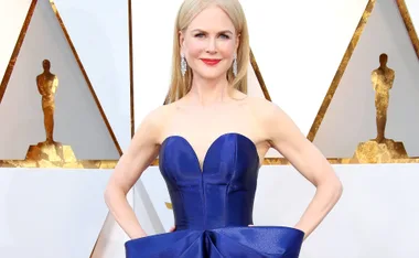 Actress in blue strapless gown at Oscars party, standing confidently with hands on hips.