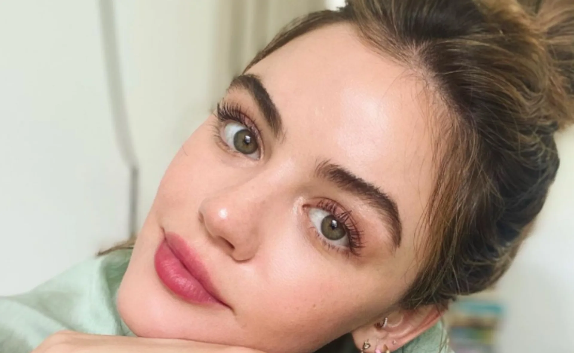 A person with laminated eyebrows, pink lips, and pulled-back hair looking into the camera.