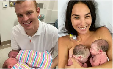 Man and woman holding newborn twins, smiling in a hospital setting.
